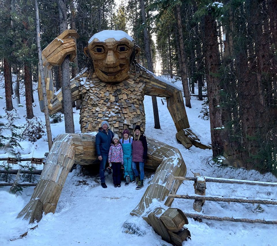 A family of four stands in front of the Breckenridge troll while enjoying Breckenridge during the winter with kids..