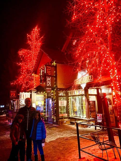 A dad and his two kids stand on a red-lit street during the holidays in Breckenridge.