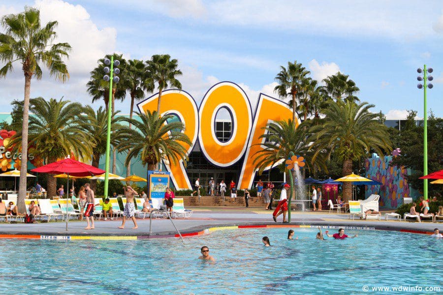 Inside Disney’s Pop Century Resort, featuring a large pool with several families enjoying a sunny day.