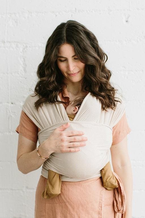 A mom holds her baby snug against her chest using a ​​Solly Baby Wrap, one of the best baby carriers for travel.