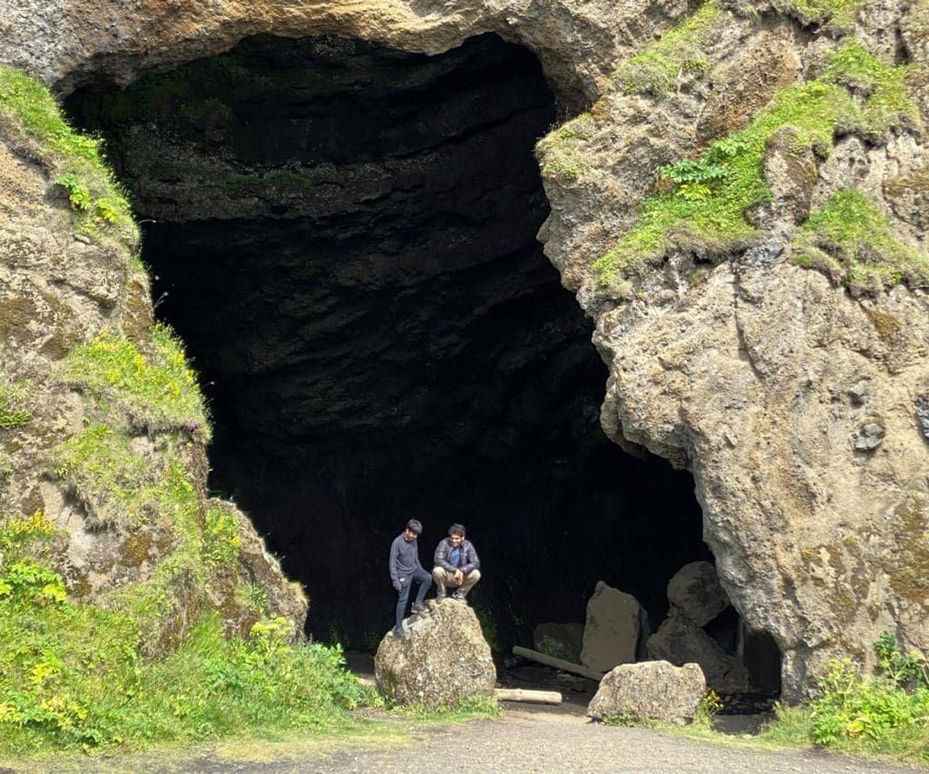 Two people explore a cave entrance at Hjorleifshofdi Cape in Iceland.
