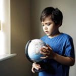 A young boy holds a globe near a window.