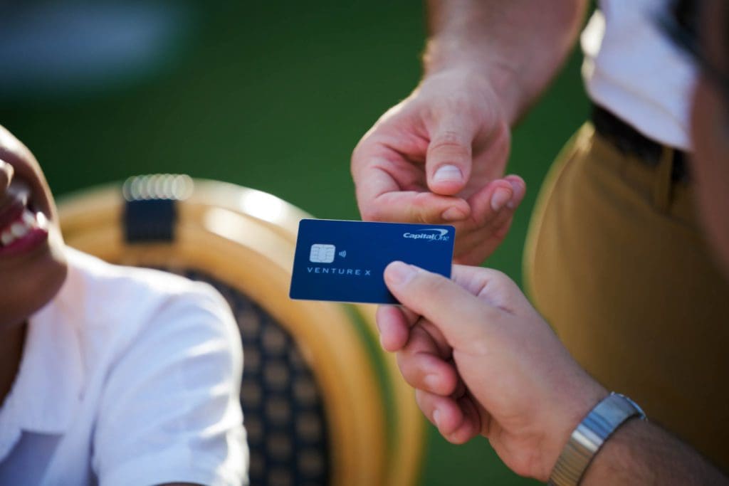 A hand reaches out to accept a Capital One Venture X Lifestyle credit card from another hand.