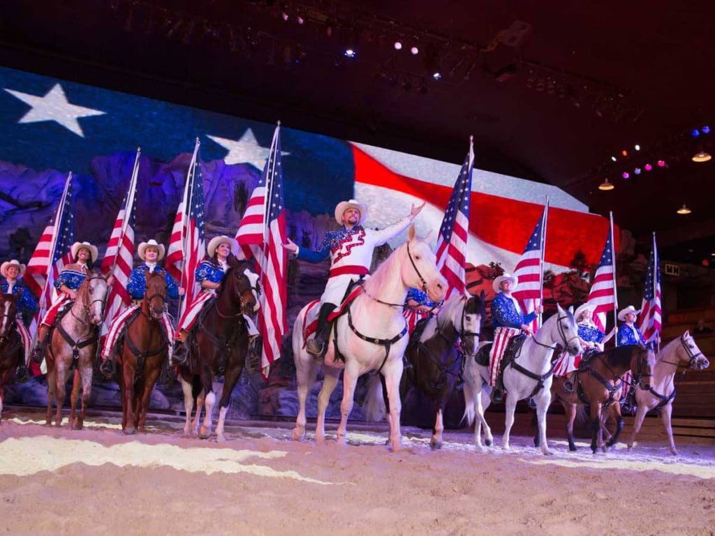 Several men on horseback, holding American flags, perform in Dolly Parton's Stampede at Pigeon Forge.