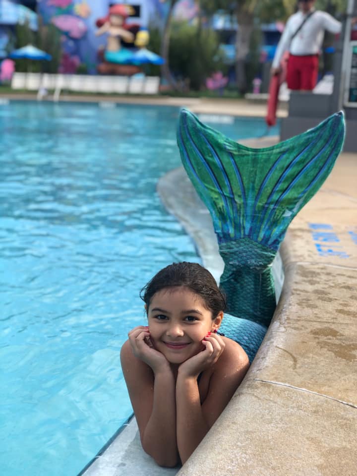 A young girl wearing a mermaid tail lays in a pool at one of the Disney Value Resorts.