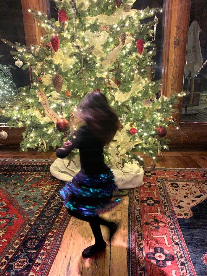 A young girl dances in front of a large Christmas tree.