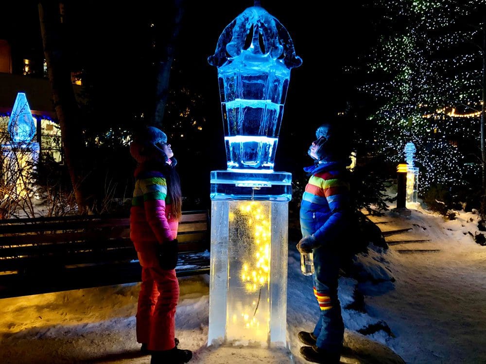 Two kids look up a a lit ice-sculpture on a dark night in Vail.