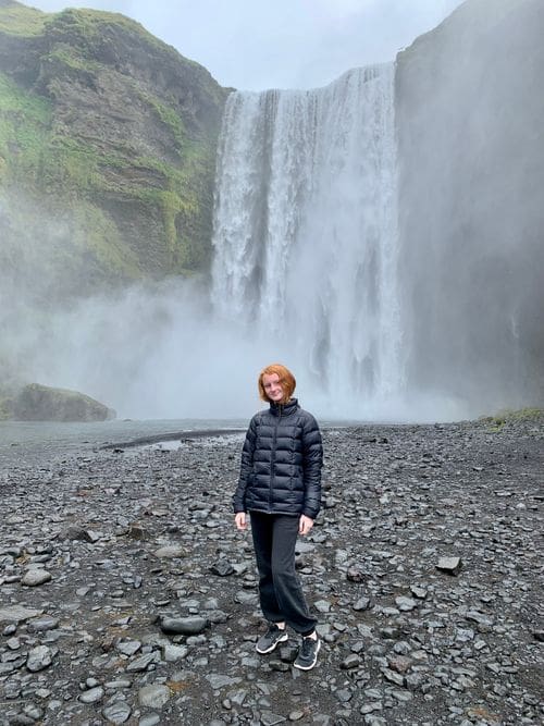 A young girl stands in front of a waterfall in Iceland.