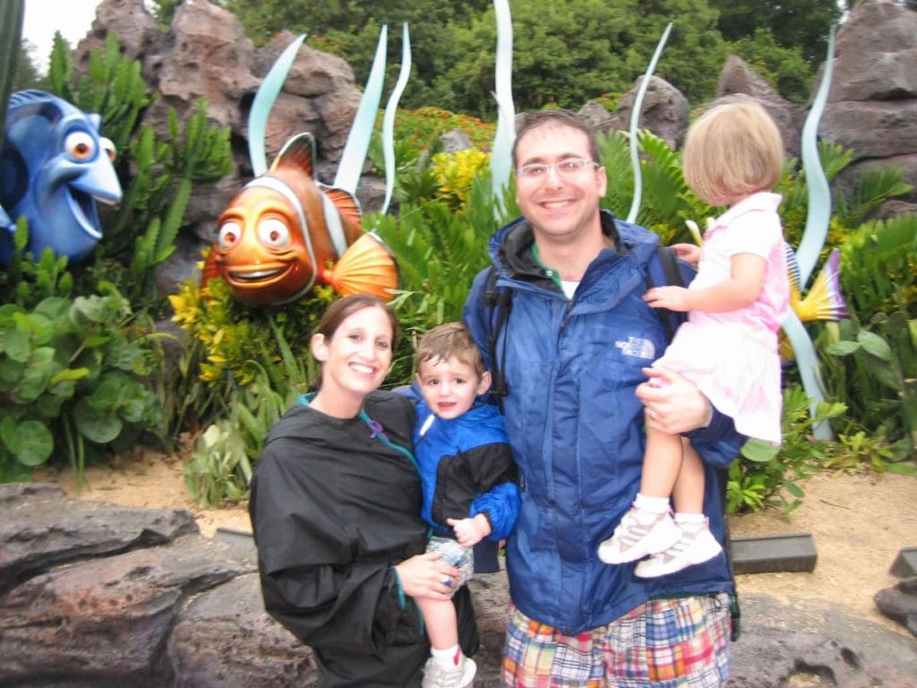 A family of four smiles as they stand together in front of two statues for Dory and Merlin from Finding Nemo.