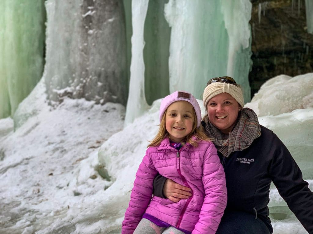 A mom and her daughter sit in front of ice flows at the Eben Ice Caves, one of the best Upper Peninsula Michigan hikes for families.