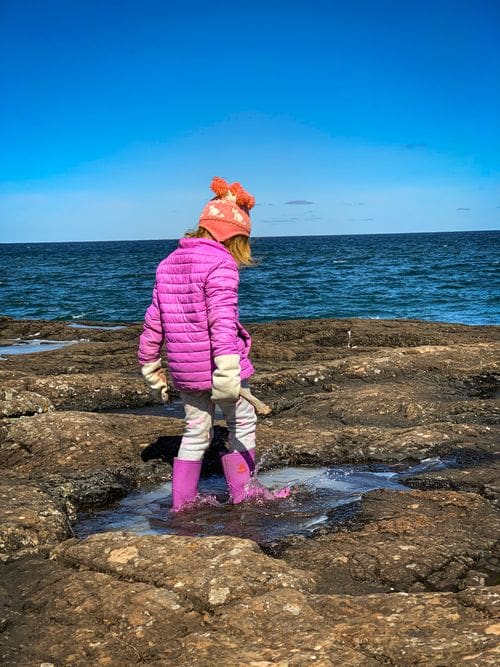 A young girl jumps in a puddle at Presque Isle Loop, with a view of Lake Superior in the distnace.