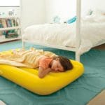 A young girl lays down on a yellow Intex Kids Travel Bed in her room.