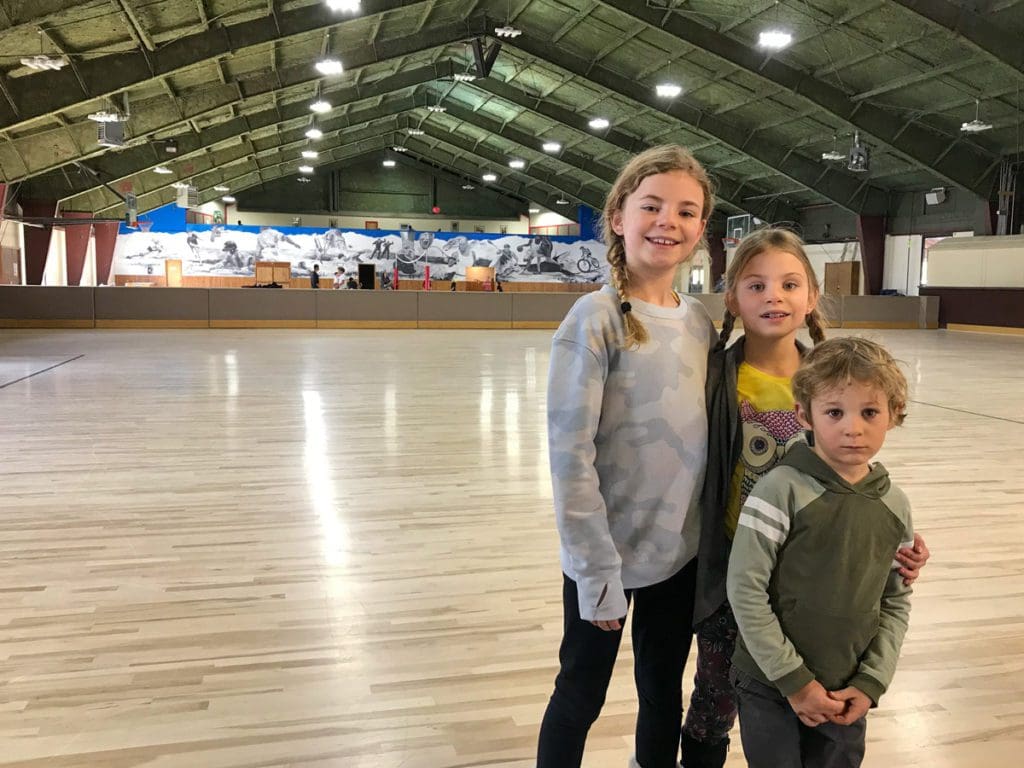 Three kids pose together inside the roller skating gym at YMCA of the Rockies.