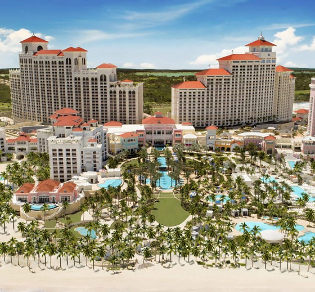 An aerial view of the hotel buildings and grounds at the SLS Baha Mar, featuring palm tree, on-site beach, and several pools.