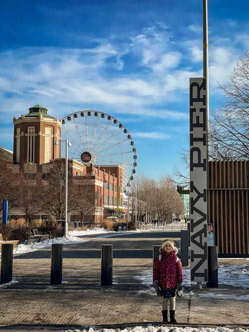 A young girl stands at the entrance of the Navy Pier, with the Centennial Wheel in the distance.