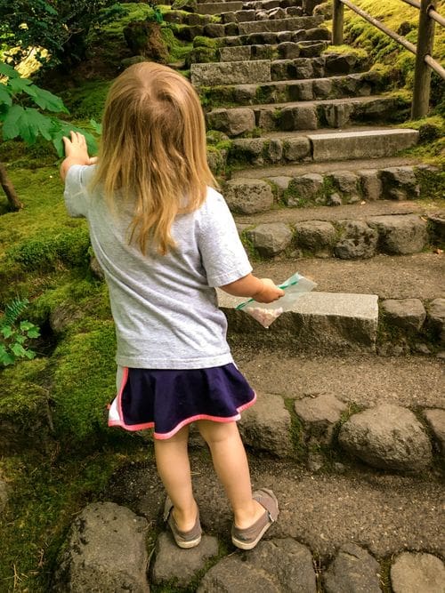 A young girl reaches up to touch a plant at the Japanese Garden in Portland.