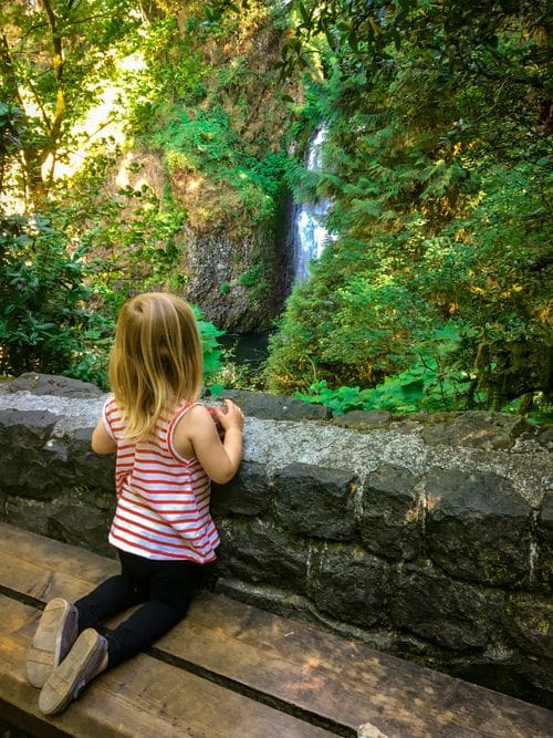 A young girl looks over a railing at Multnomah Falls, one of the best things to do in Portland with kids.