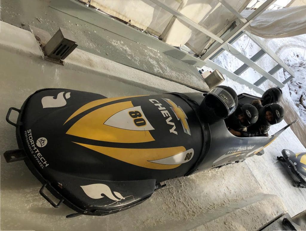 Two kids sit inside a yellow and black bobsled.