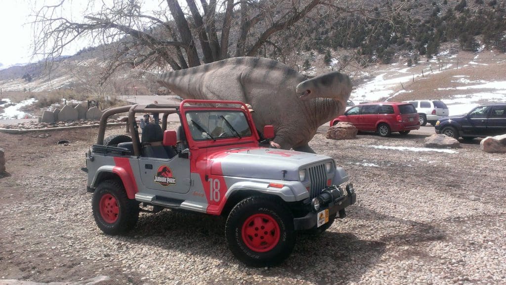 A Jurassic Park vehicle is parked near a dinosaur display at Dinosaur Ridge.
