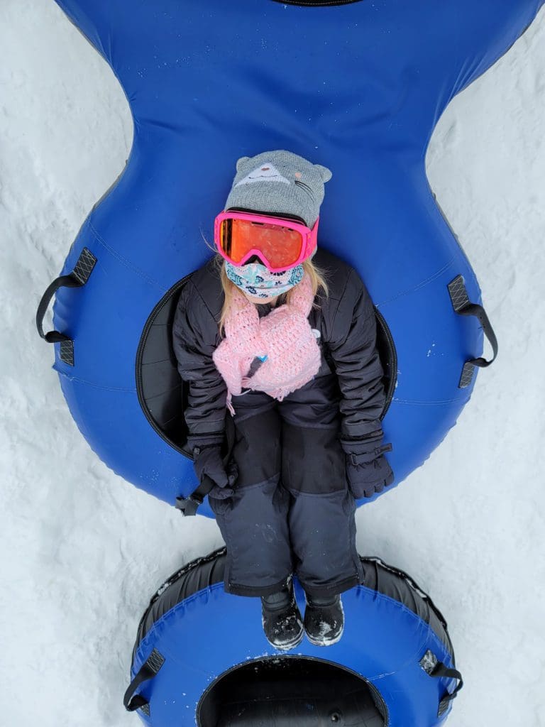 A young girl looks up at a camera while riding a blue snow tube down a snowy slope at Camelback Resort.