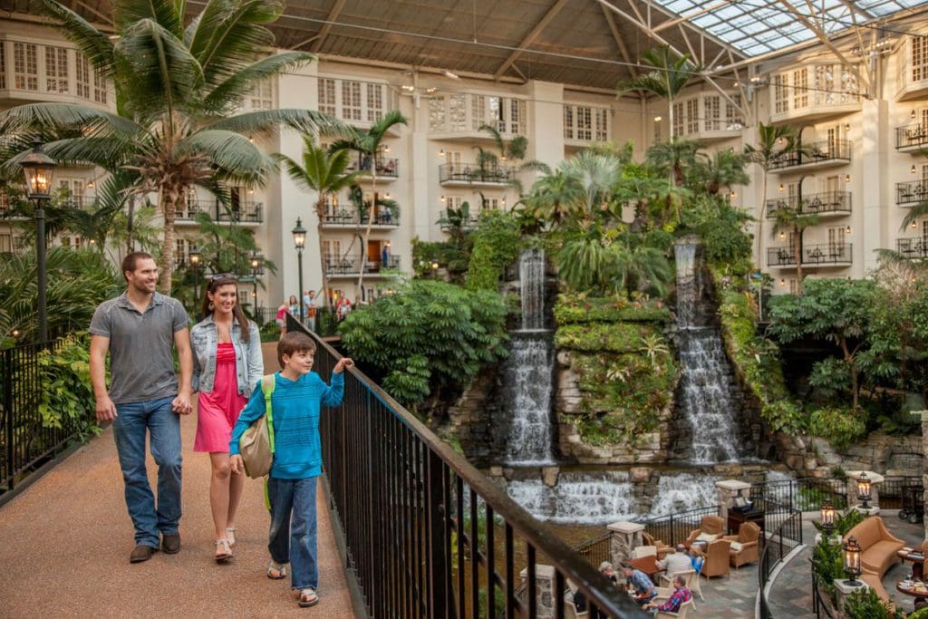 Two parents and their young son walk across the boardwalk within the atrium at the Gaylord Opryland Resort & Convention Center, with an indoor waterfall in the distance.