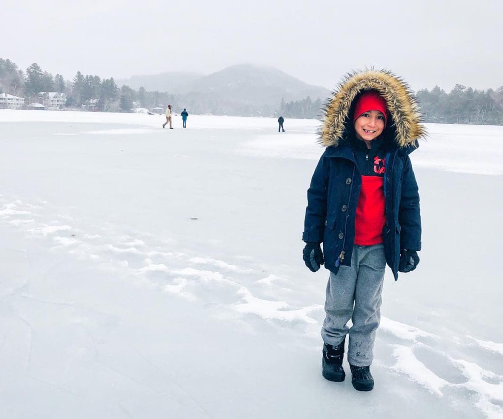 A young boy in a winter coat stands on a frozen lake in Lake Placid.