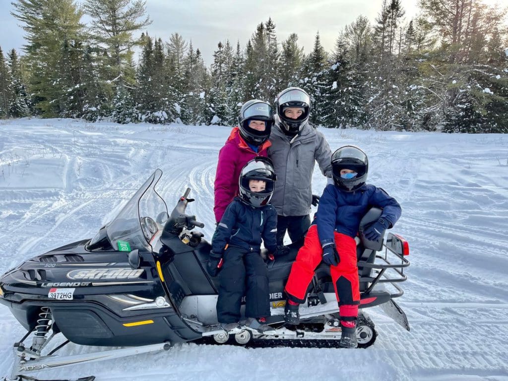 A family of four stands together near a snowmobile, while exploring trails near Lake Placid.