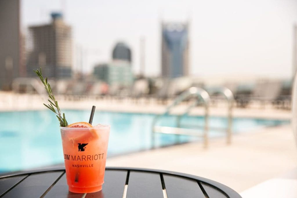 A cup reading "The JW Marriott Nashville" sits on a poolside table, with the outdoor pool behind it.