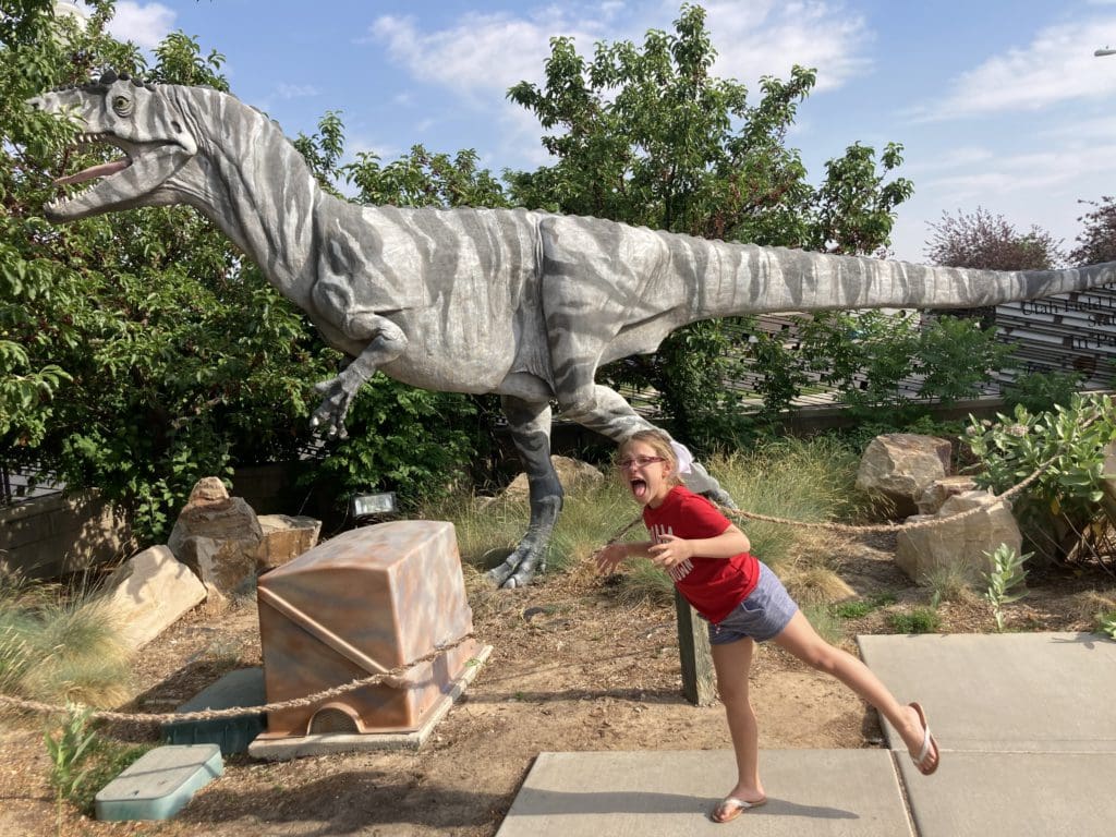 A young girl pretends to look like the dinosaur behind her while exploring the Field House Natural History Museum in Utah, one of the best places for a dinosaur-themed vacations in the united states for families.