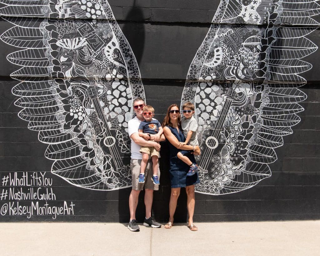 A family of four stands together in front of the iconic angel wings street mural in Nashville.