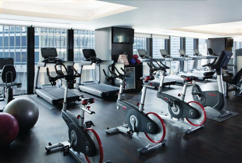 Inside the fitness center at The Langham, Chicago, featuring treadmills, stationary bikes, fitness balls, and a Chicago skyline view.