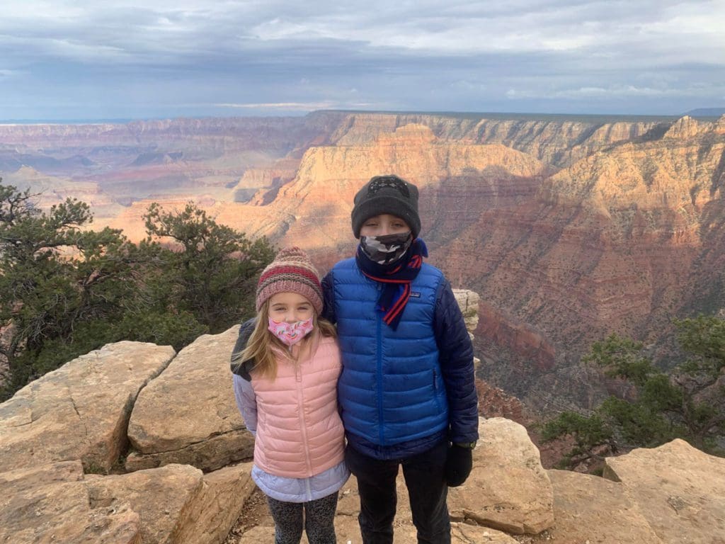 Two kids stand together at the top of the Grand Canyon, with an expansive view of the area behind them.