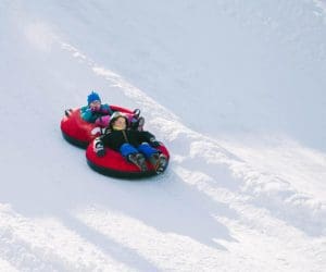 Two kids ride tandem on a snow tube in the snow at Mountain Creek Ski Resort.
