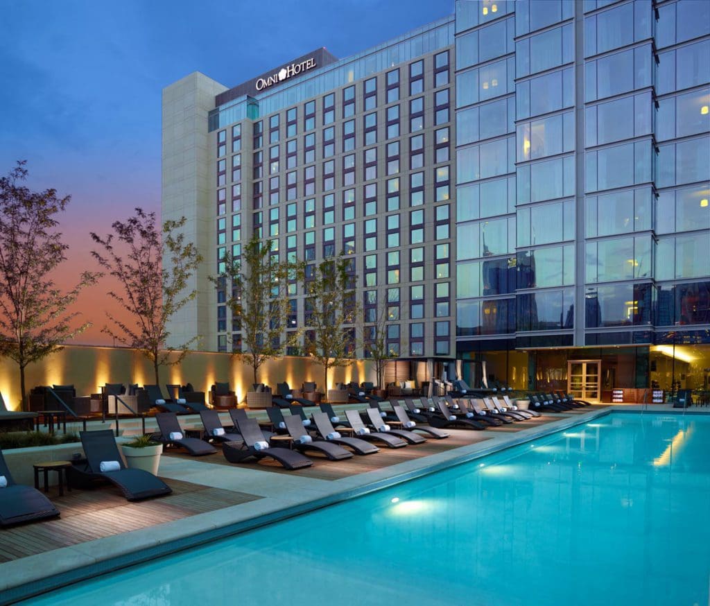 A view of the pool and poolside loungers at the Omni Nashville Hotel at night, while the hotel stands in the background.