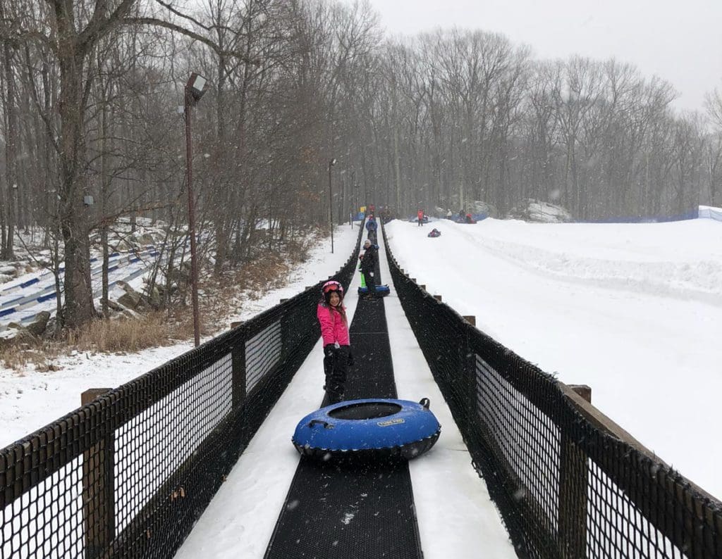 A young girl pulls a snow tube up a magic carpet at Rocking Ranch, one of the best hotels with snow tubing near NYC for families.
