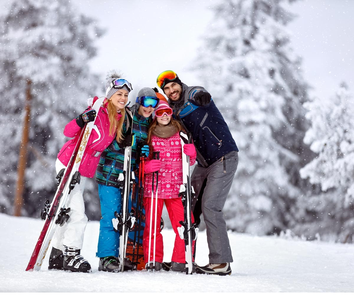 A family of four, all wearing colorful ski gear and skis, stands proudly on a winter landscape near Aspen.