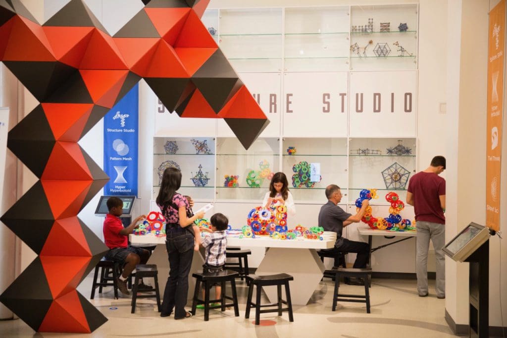 Several parents and their children play at an exhibit at National Museum of Mathematics, one of the best museums in New York City for kids.