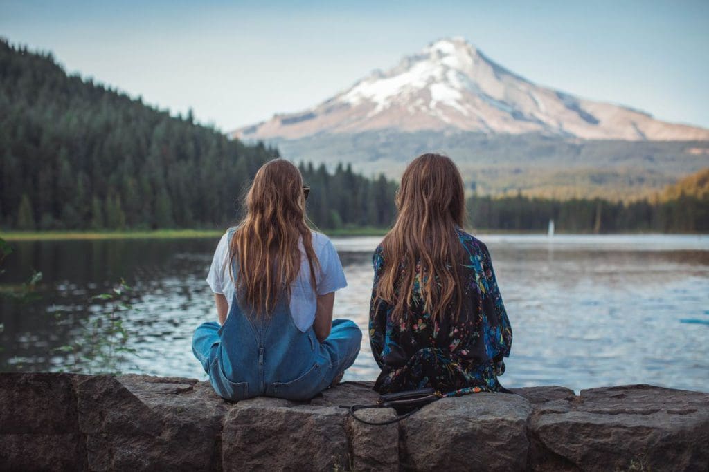 Two girls sit on a brick wall, with Mount Hood in the distance.