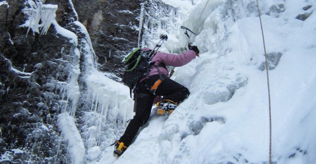 An ice climber with a pick and ropes scales a wintery mountainside.