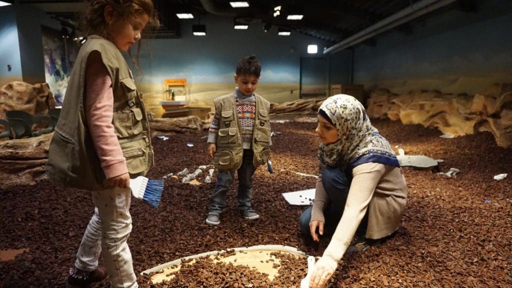 Two kids and their mom play in an interactive dinosaur dig exhibit at the Chicago Children's Museum, one of the best dinosaur museums in the United States for families.