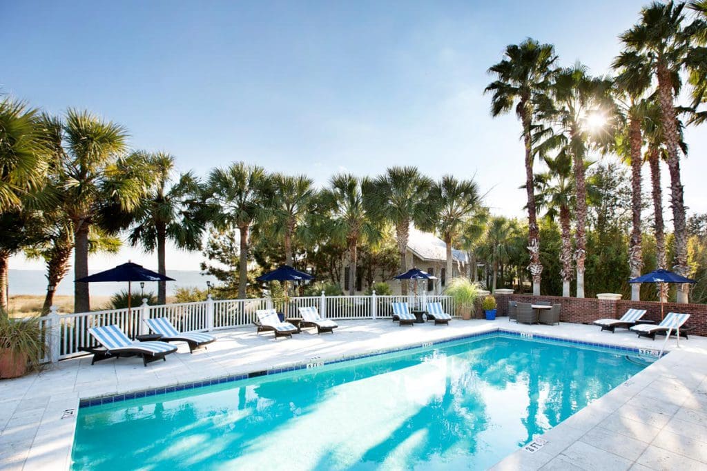 The outdoor pool at The Cottages on Charleston Harbor, flanked by swaying palm trees on two sides.
