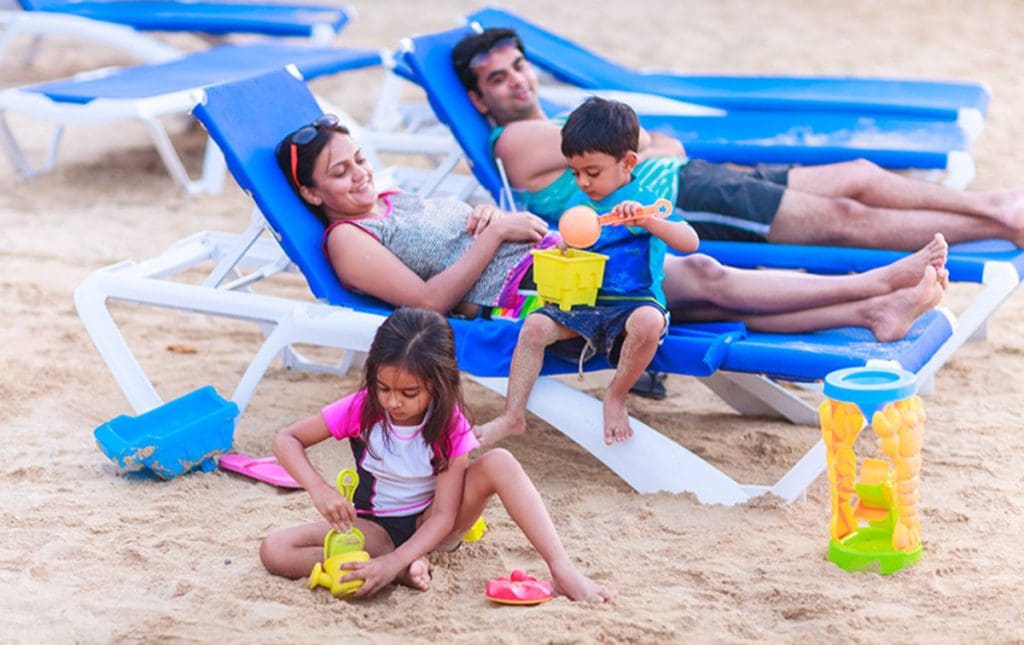 Two parents sit on beach loungers, while their kids play in the sand nearby at Franklyn D. Resort & Spa.