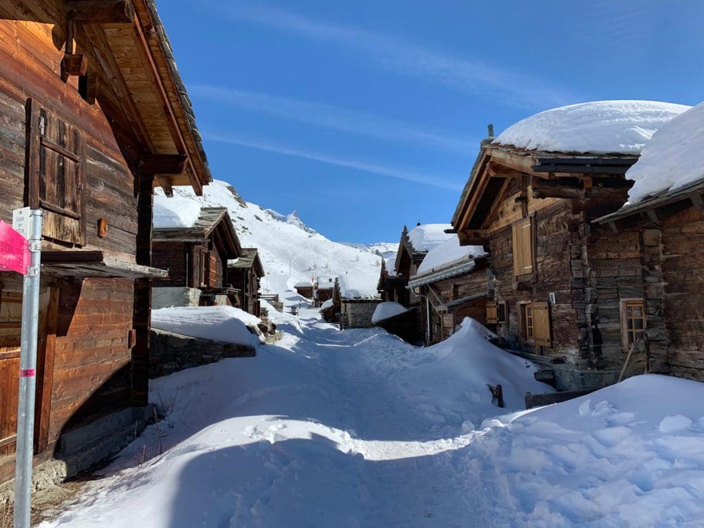 Old buildings line a snowy street as part of an abandoned area you can explore while hiking near Zermatt with kids.