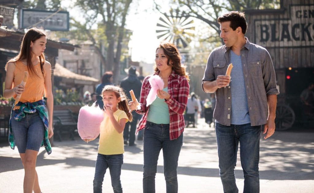 A family of four walks along the theme park associated with Knotts Berry Farm Hotel, eating cotton candy and other treats.