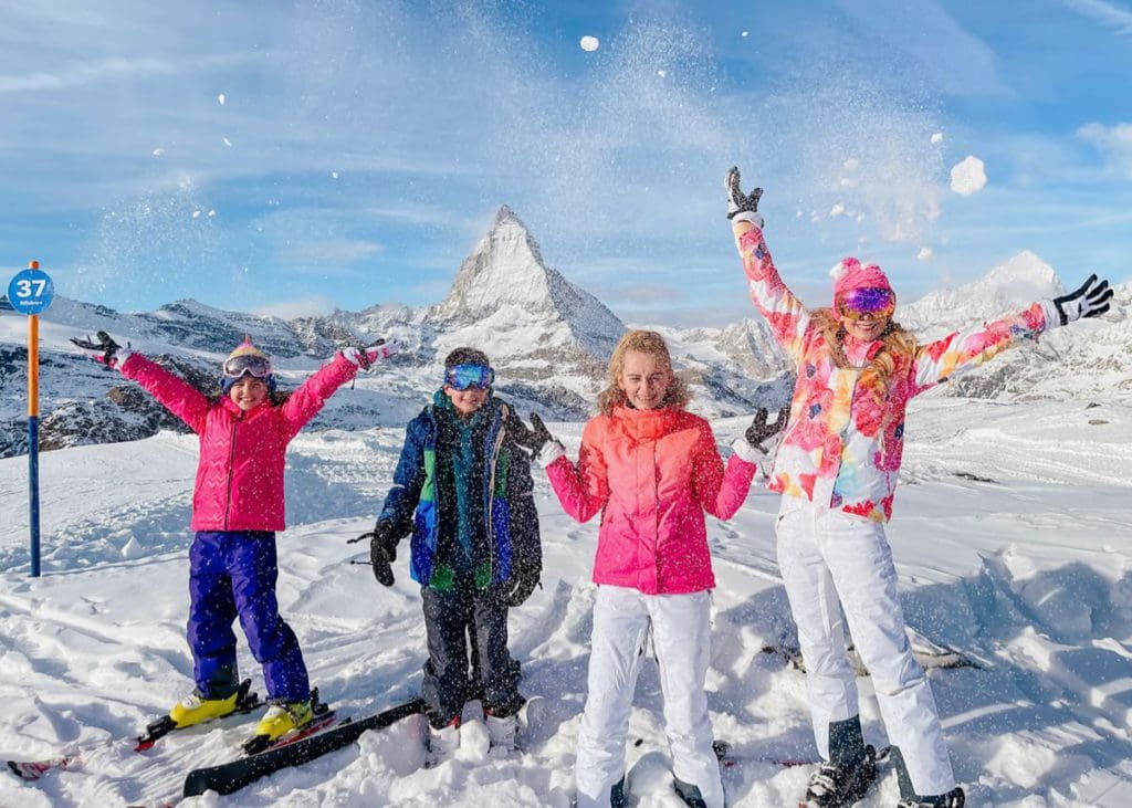 A mom and her three kids throw snow in the air, while skiing in Zermatt together.
