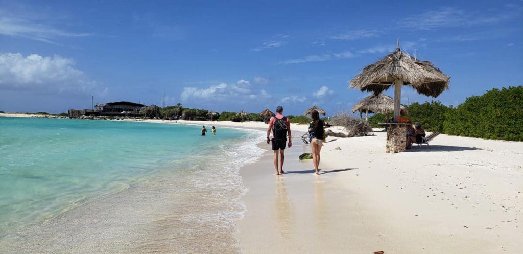 A couple walks across a beach near the water, while exploring Baby Beach in Aruba.