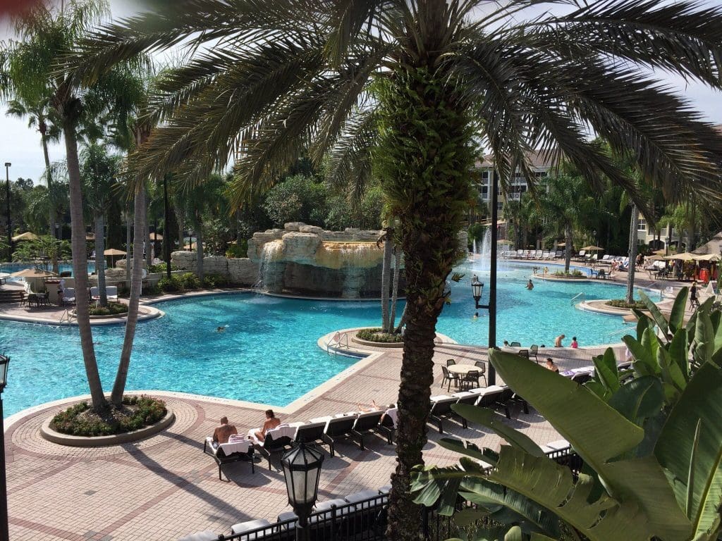 The pond and surrounding pool deck at Sheraton Vistana Resort Villas, with sway palm trees and poolside loungers, one of the Best Marriott Properties in the U.S. for a Family Vacation.