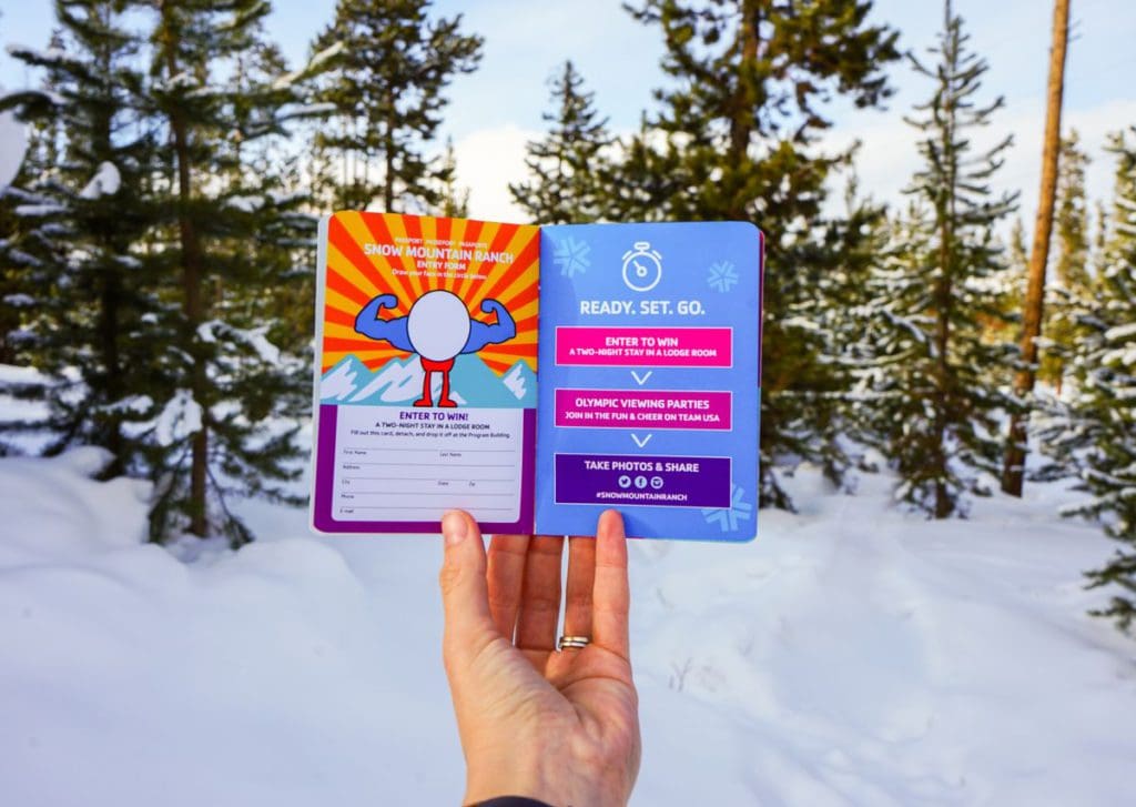 A hand holds a small passport-style book for the Winter Olympics event at Snow Mountain Ranch.