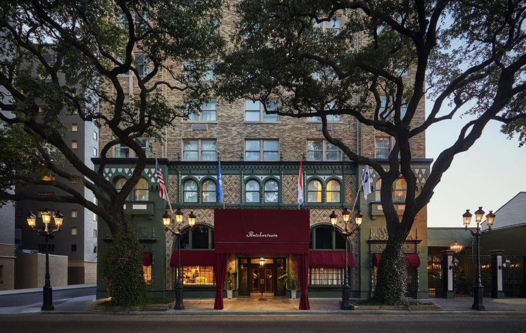 The shaded entrance to The Pontchartrain Hotel, featuring large trees and a grand entrance area.