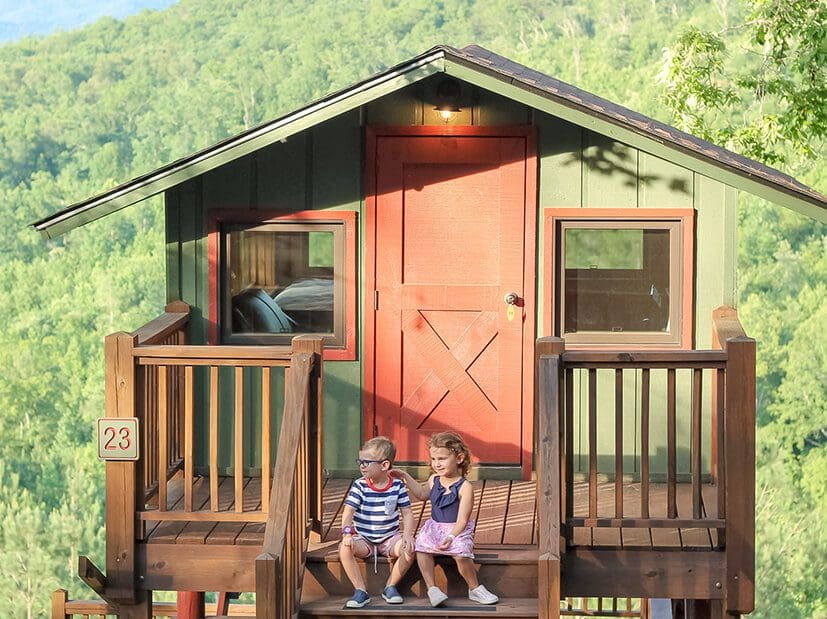 Two kids sit outside a cozy cabin at one of the Jellystone Parks.